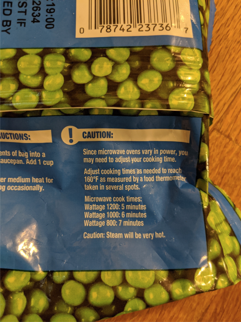 Instructions on a bag of frozen peas indicating the importance of microwave wattage for safe cooking